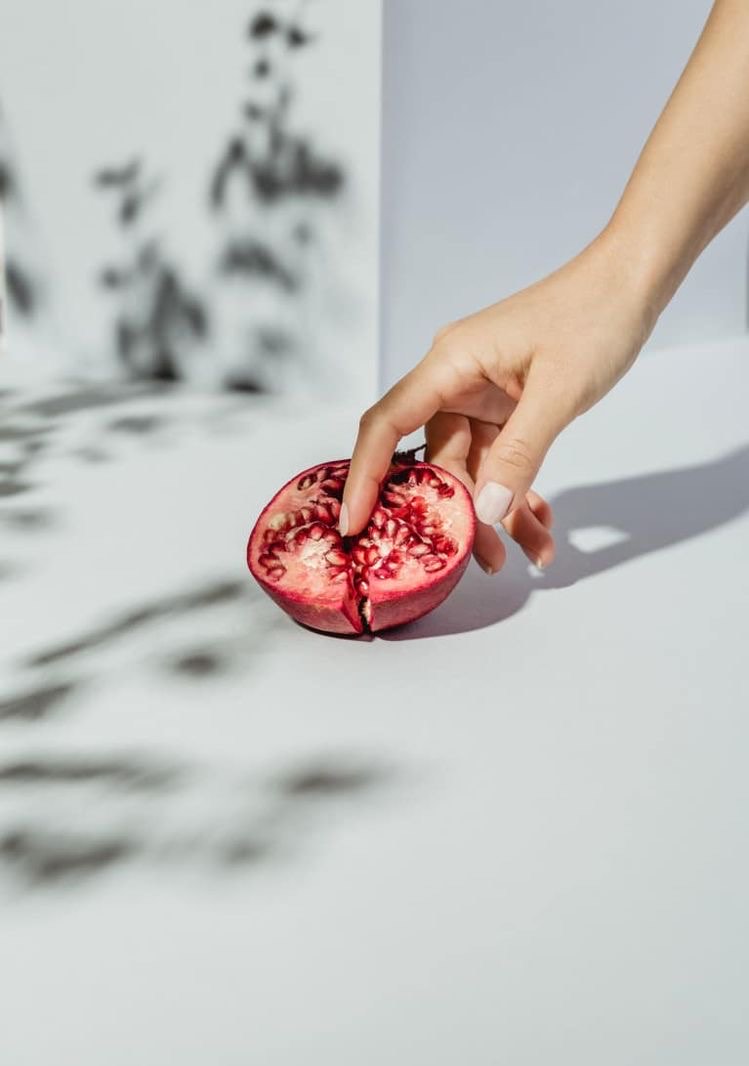 a woman's hand holding a pomegranate on a white background